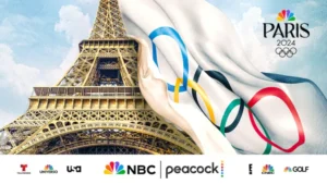 The Eiffel Tower has a large olympic flag drapped over it while NBC logos are seen on the bottom of the image.