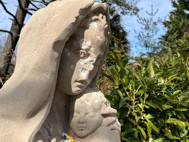 A statue of the Virgin Mary and baby Jesus is shown with large marks and divots from damage.