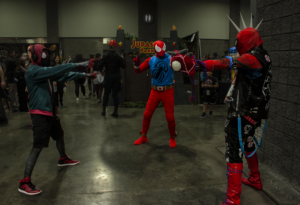 Three men stand in spiderman suits pointing at each other.